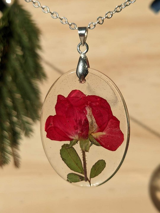 Collier ovale transparent en résine contenant une véritable rose